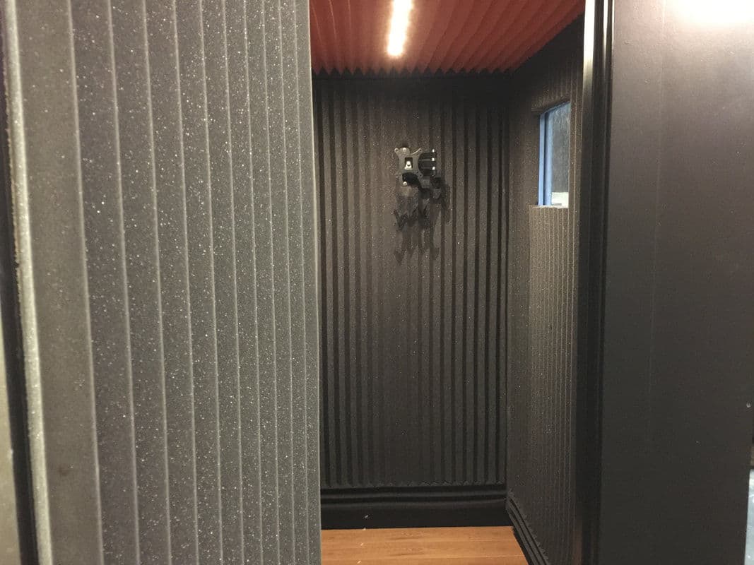 Soundproof recording booth interior with acoustic panels and a hanging mic holder.