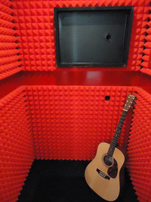 Acoustic sound booth with red foam panels and an acoustic guitar on the floor.