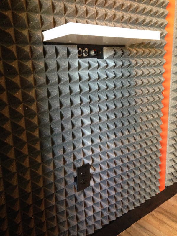 Acoustic foam wall panel with shelf and electrical outlets in a soundproof studio.