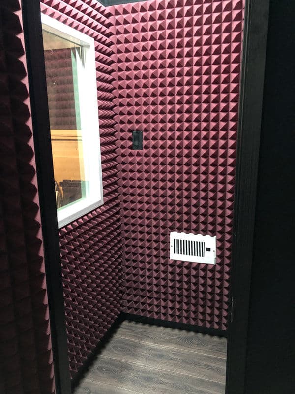 Soundproof recording booth with acoustic foam panels and a window for monitoring.
