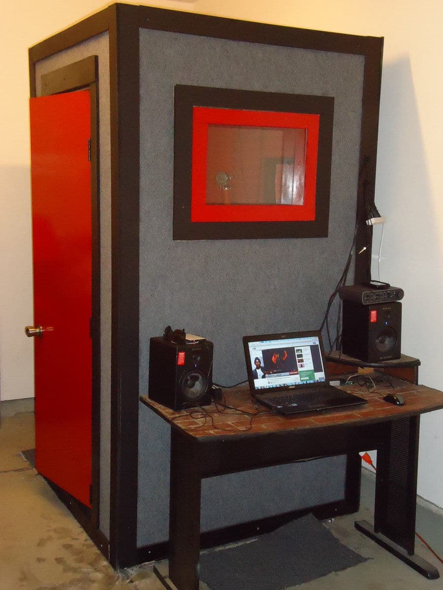 Soundproof recording booth with computer and speakers, ideal for audio production and music.