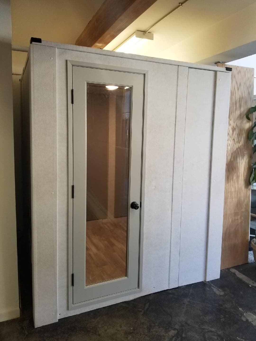 Soundproof booth with a glass door and wood flooring, designed for quiet spaces.