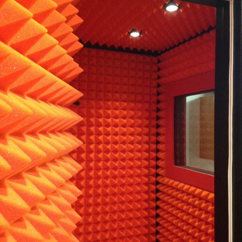 Soundproof studio room with bright orange acoustic foam walls and a viewing window.
