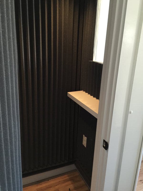 Soundproof phone booth with ribbed black walls and a small shelf inside.