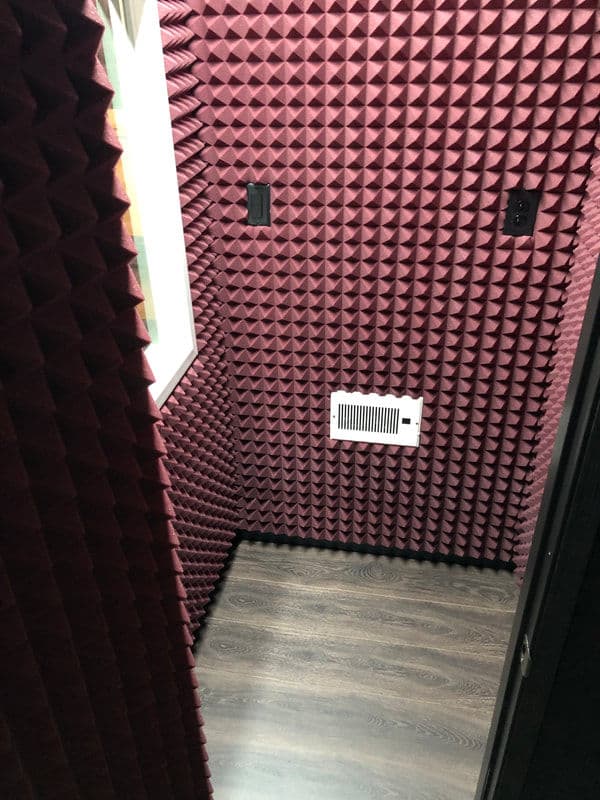 Soundproof recording booth with purple acoustic foam panels and a wooden floor.