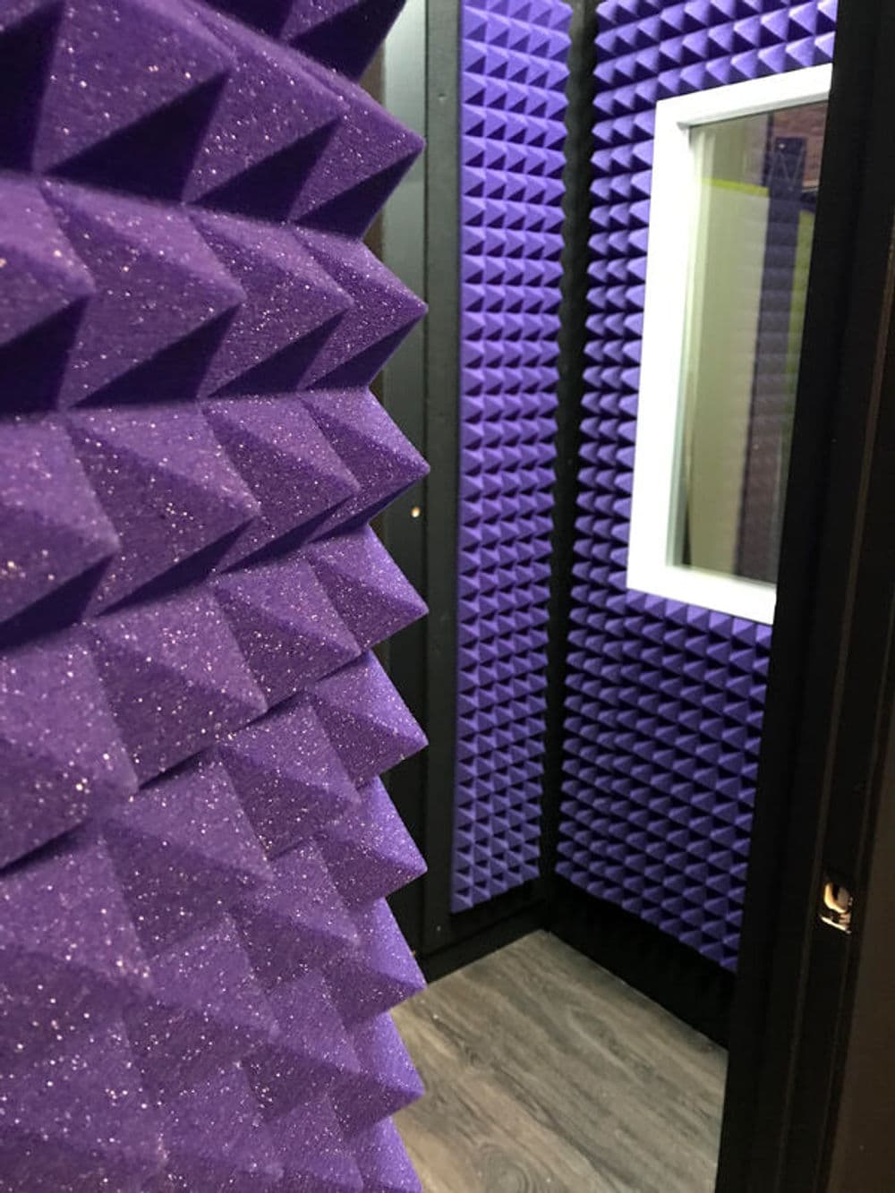 Soundproof recording studio with purple acoustic foam panels and a view window.