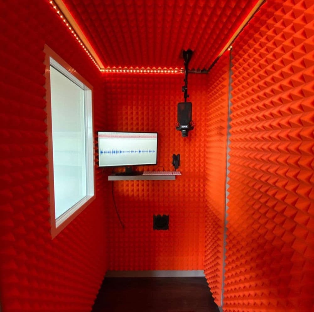 Soundproof recording booth with vibrant orange acoustic foam and microphone setup.