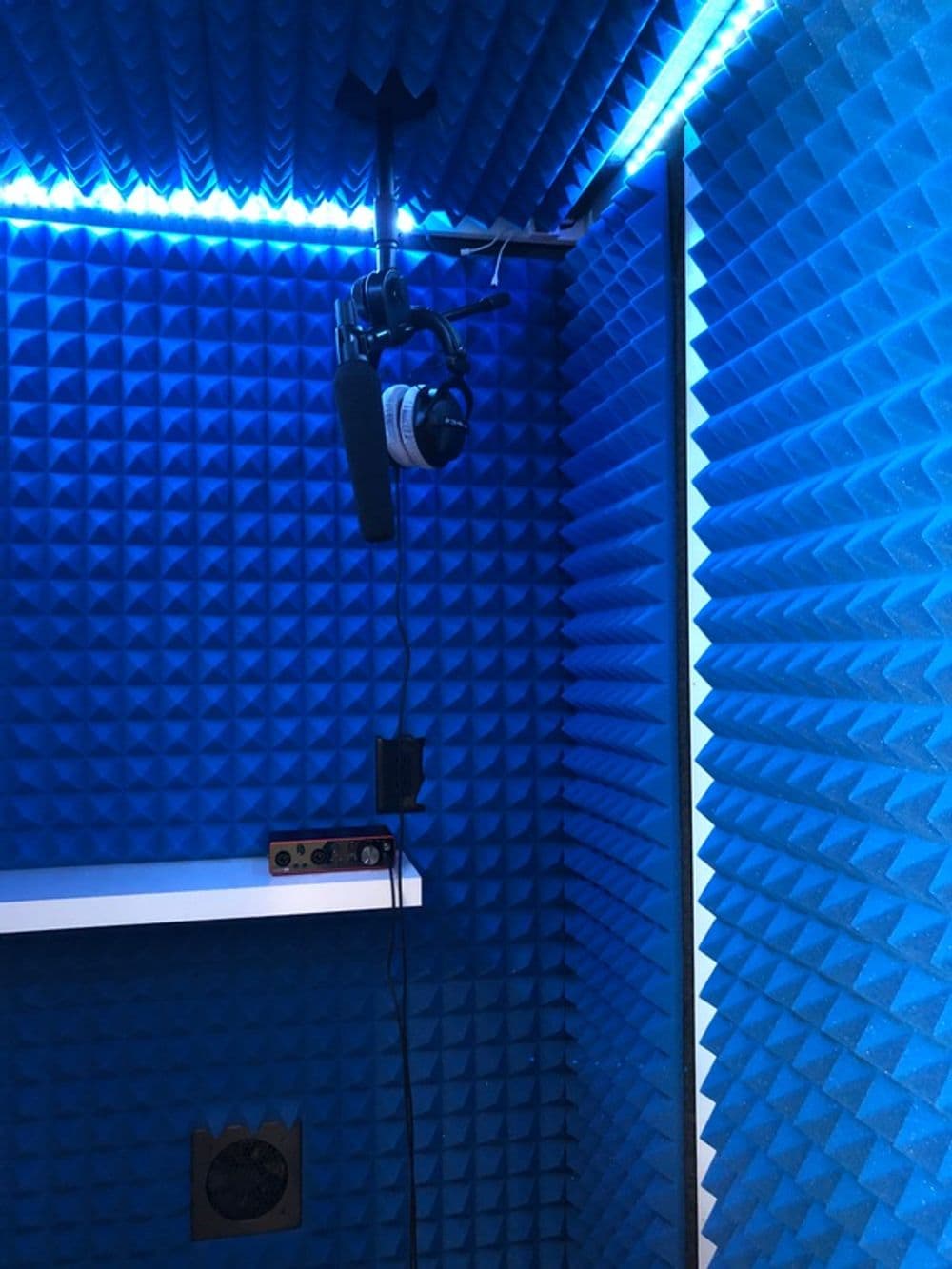 Soundproof recording booth with blue acoustic foam, microphone, and headphones.